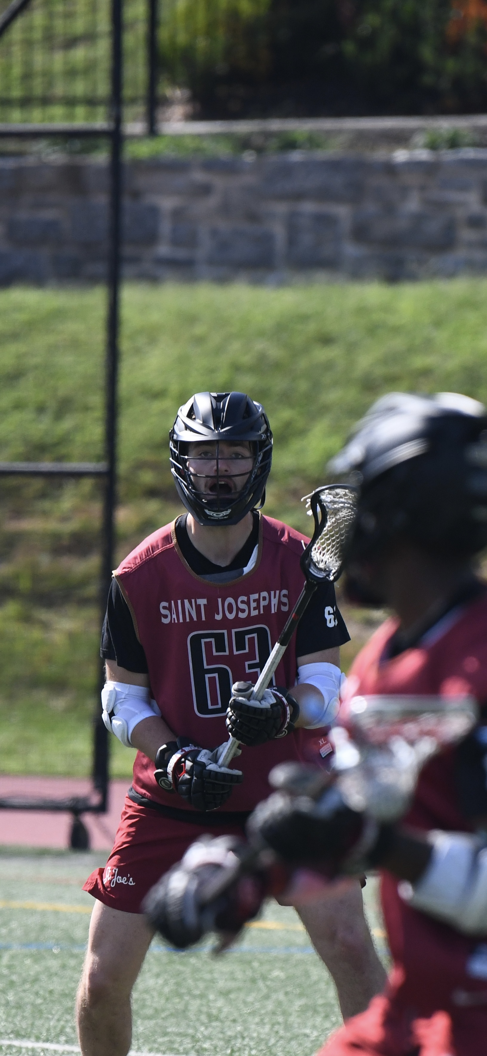 Saint Joe's lacrosse player wearing a black helmet, red pinny, red shorts, and black undershirt